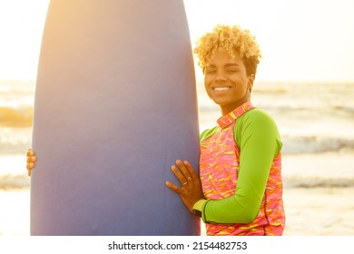 Latin Hispanic Woman With Blonde Afro Curls Holdian A Surfboard On Beach