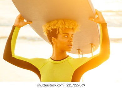 Latin Hispanic Woman With Blonde Afro Curls Holdian A Surfboard On Beach