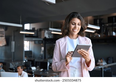 Latin Hispanic young professional business woman working on touchscreen computer. Middle eastern Indian businesswoman CEO holding digital tablet using tab application standing at workplace in office - Powered by Shutterstock