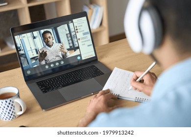 Latin Indian Adult Student Wearing Headset Having Virtual Meeting Online Call Training Educational Webinar Chatting With Black Teacher At Home Office Using Laptop. Over Shoulder View.