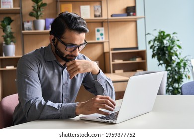 Latin Indian Serious Businessman Wearing Glasses And Headset Having Virtual Team Meeting Call, Remotely Working At Home Watching Online Learning Training Webinar In Remote Office.