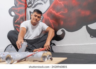 Latin male young artist picking an aerosol from floor painting a new mural - Powered by Shutterstock