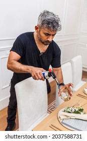 Latin Man Lighting A Candle With A Blowtorch. Chef Preparing The Table For A Private Dinner Party.