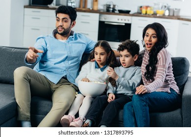 Latin Man Pointing With Finger While Watching Tv With Hispanic Family At Home