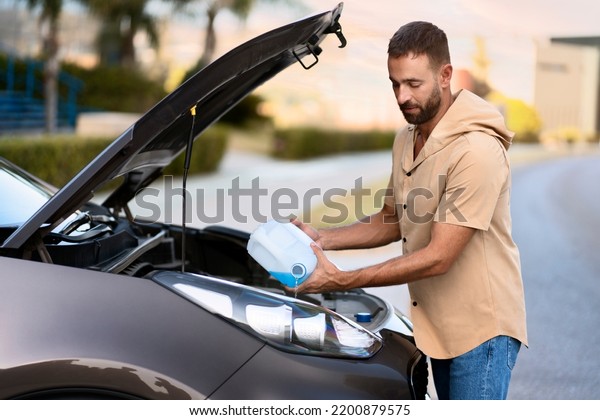 Latin man pouring windshield washer fluid\
for clearing car. Car service concept\
	\
