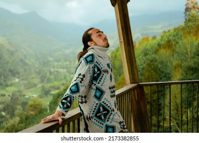 latin man in a ruana dress on a balcony meditating with a relaxing colombian coffee landscape, being present