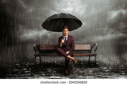 Latin man sitting on a bench with umbrella in the rain in the middle of a stormy night, horizontal - Powered by Shutterstock