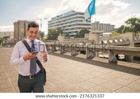 Latin man with a tie walking through the financial center of Guatemala with his cell phone and a coffee cup in his hands. Buildings and flag of Guatemala in the background. ストックフォト © 