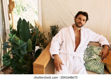 Latin Man In White Bathrobe Rests Sitting On Couch After Baths Procedures And Wellness At Spa Resort