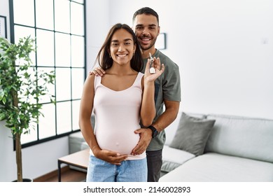 Latin man and woman couple hugging each other holding key of new house expecting baby at home - Powered by Shutterstock