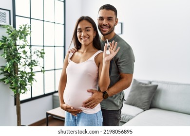 Latin man and woman couple hugging each other holding key of new house expecting baby at home - Powered by Shutterstock