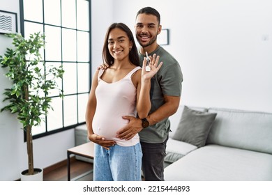 Latin man and woman couple hugging each other holding key of new house expecting baby at home - Powered by Shutterstock