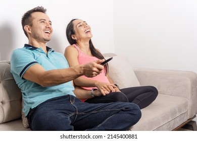 Latin Man And Woman Couple Watching Tv, Laughing And Using Remote Control