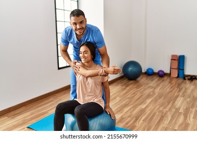 Latin man and woman wearing physiotherapist uniform having rehab session using fit ball at rehab center - Shutterstock ID 2155670999