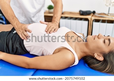 Latin man and woman wearing physiotherapist uniform having pregnancy rehab session massaging belly at physiotherapy clinic