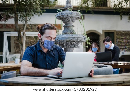 latin man working with computer wearing face mask for social distancing in new normal situation protecting and preventing the infection of corona virus or covid-19, mexican coworkers in Mexico city