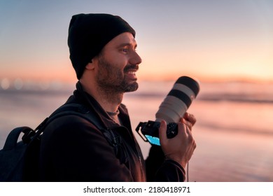 latin mature photographer holding professional camera on the beach and smiling happy portrait