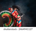 Latin Mexican couple with Jalisco, charro costumes A man and woman in traditional Mexican clothing are dancing together. The man is wearing a sombrero and the woman is wearing a colorful skirt. 