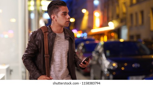 Latin Millennial Guy On City Street At Night Hailing A Cab Or Rideshare Car