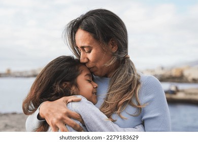 Latin mother and daughter having tender moment on the beach - Loving mom kissing her child outdoor - Family love concept - Powered by Shutterstock