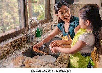 Latin Mother and Daughter. The mother teaches her daughter to wash the dishes they share moments together and have fun. - Shutterstock ID 2169622405