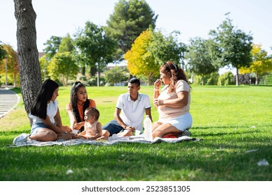 Latin multigenerational family with a baby having a picnic outdoors on a sunny day - Powered by Shutterstock