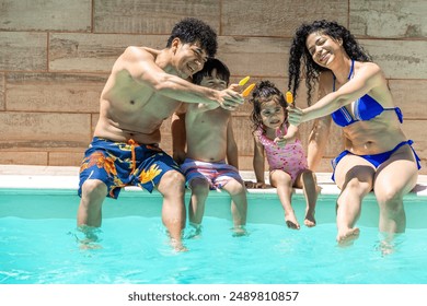 latin parents and children enjoy popsicles while sitting on the pool edge, smiling and dipping their feet in the water. They relax and enjoy the sunny day. - Powered by Shutterstock