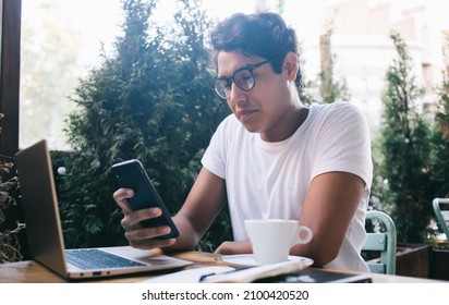 Latin IT professional in optical eyeglasses making online banking of paid subscription for application sitting at street cafe with laptop for distance working,skilled male connecting to 4g on cellular