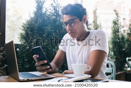 Latin IT professional in optical eyeglasses making online banking of paid subscription for application sitting at street cafe with laptop for distance working,skilled male connecting to 4g on cellular