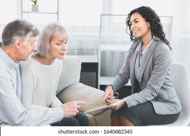 Latin Real Estate Agent Showing House Plans On Electronic Digital Tablet, Senior Couple Looking At Apartment Floor Plan