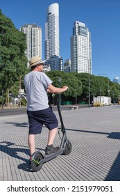 Latin senior man riding his electric kick scooter around the city in summer. Concepts of sustainability, summer tourism, active life, clean energy and green mobility, eco transportation. - Shutterstock ID 2151979051