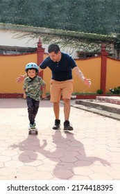 Latin Single Dad Teaches His Son To Ride A Skateboard With A Helmet Very Funny And Happy Of The Achievement Of Learning Something New
