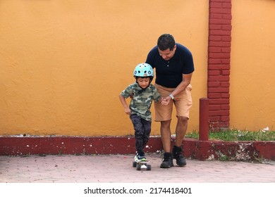 Latin Single Dad Teaches His Son To Ride A Skateboard With A Helmet Very Funny And Happy Of The Achievement Of Learning Something New
