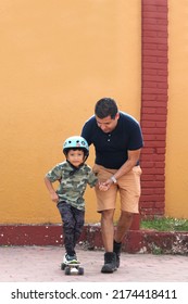 Latin Single Dad Teaches His Son To Ride A Skateboard With A Helmet Very Funny And Happy Of The Achievement Of Learning Something New
