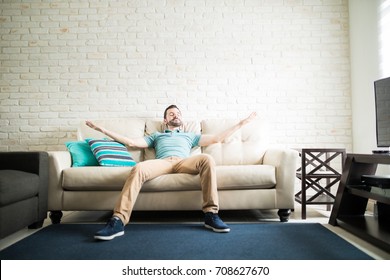 Latin Single Man Relaxing Alone In The Living Room Of His New Apartment With Her Arms Open