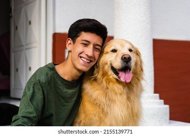 latin teenager laughing and hugging his golden retriever dog sitting in the driveway - Powered by Shutterstock