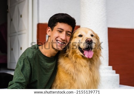 latin teenager laughing and hugging his golden retriever dog sitting in the driveway