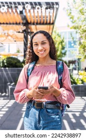 Latin university student woman smiling and using her mobile sitting outside the campus in free time - Shutterstock ID 2242938897