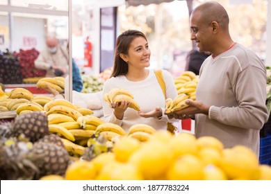 Latin wife choosing sweet bananas in supermarket and husband near helping her