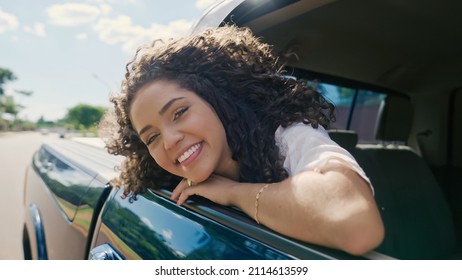 Latin woman in car window. Car trip. Curly hair in wind. Girl looks out of car window.