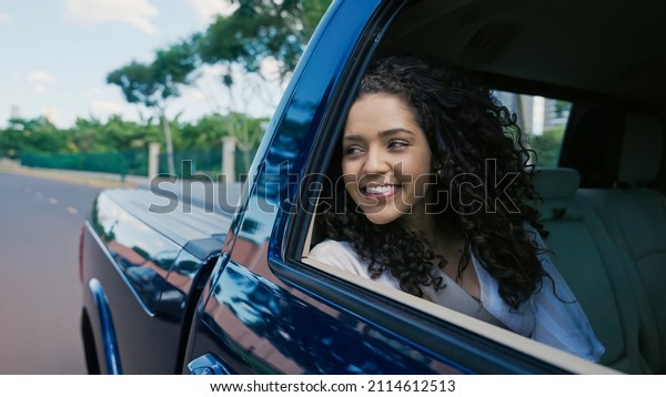 Latin woman in car window. Car trip. Curly\
hair in wind. Girl looks out of car\
window.