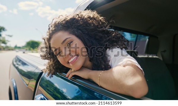 Latin woman in car window. Car trip. Curly\
hair in wind. Girl looks out of car\
window.