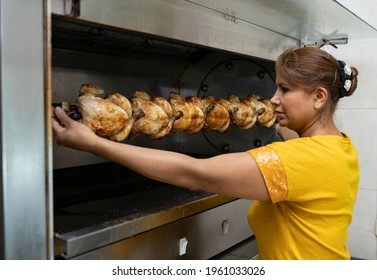 Latin Woman Cooking Rotisserie Chicken In A Large Oven