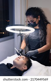 latin woman cosmetologist outlining a man's eyebrows before micropigmentation - Shutterstock ID 2170449569