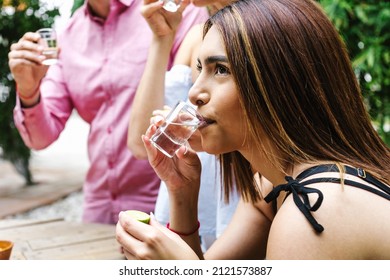 Latin Woman drinking tequila or mezcal shot with group of young latin Friends making A Toast In Restaurant terrace in Mexico Latin America