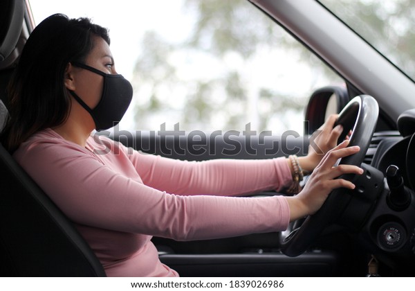 \
latin woman driver with protection mask in\
vehicle interior, new normal when\
driving