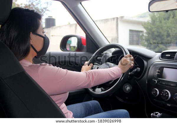 \
latin woman driver with protection mask in\
vehicle interior, new normal when\
driving