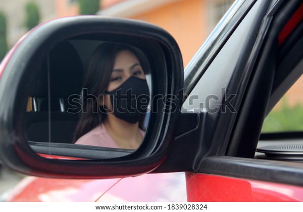 \
latin woman driver with\
protection mask inside red car, view in mirror new normal when\
driving