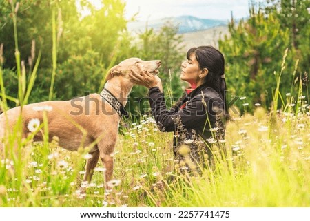 Latin woman and her dog together. Friendship between dog and pet owner. Woman sitting with her greyhound in nature.