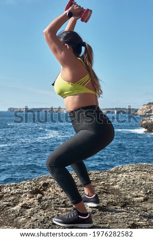 Latin woman, middle-aged, resting, regaining strength, eating, drinking water, after a gym session, burning calories, keeping fit, outdoors by the sea, wearing headphones and smart watch